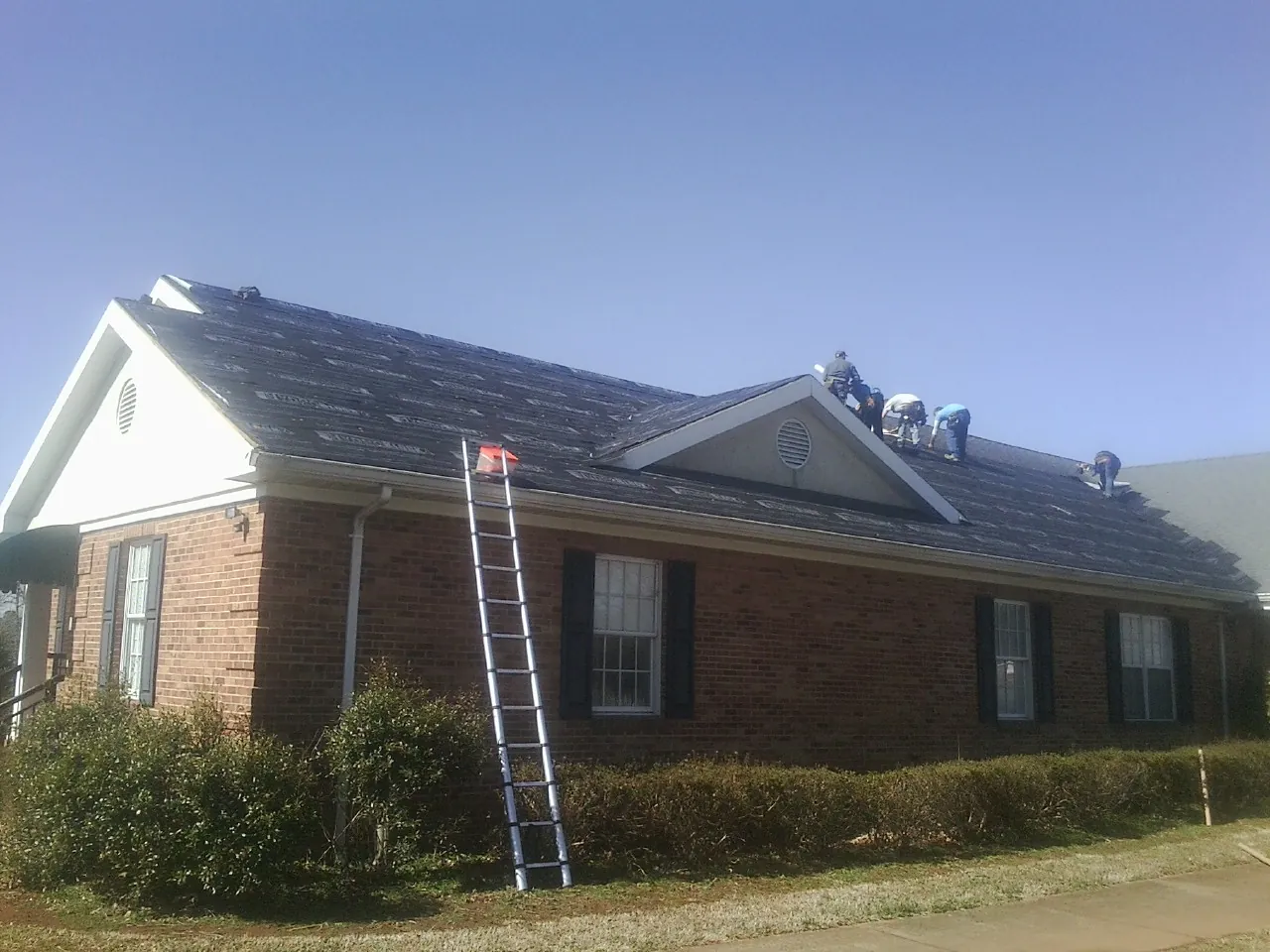 Crew tearing shingles off a brick ranch roof with a ladder set — Metal Roof Repair work by our crew in Freeport